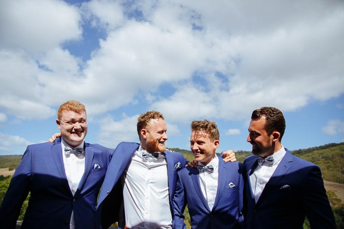 Four men in royal-blue wedding jackets stand shoulder to shoulder