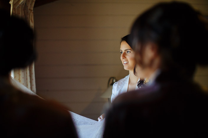 The bride smiles as attendants in robes hold up her wedding gown