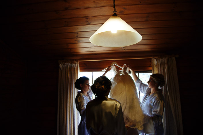 Three attendants lift the beaded wedding gown towards a cottage window at Pennyroyal Otways Retreat