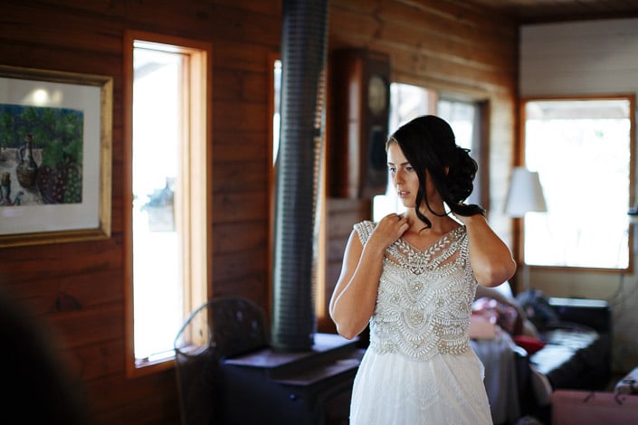 The bride adjusts her neckline beside the wood stove in a Pennyroyal Retreat cottage