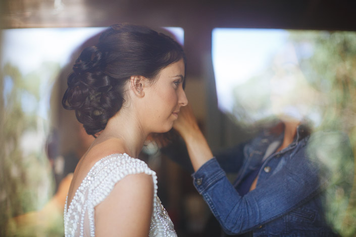 A stylist in a denim jacket tends the bride's curled updo