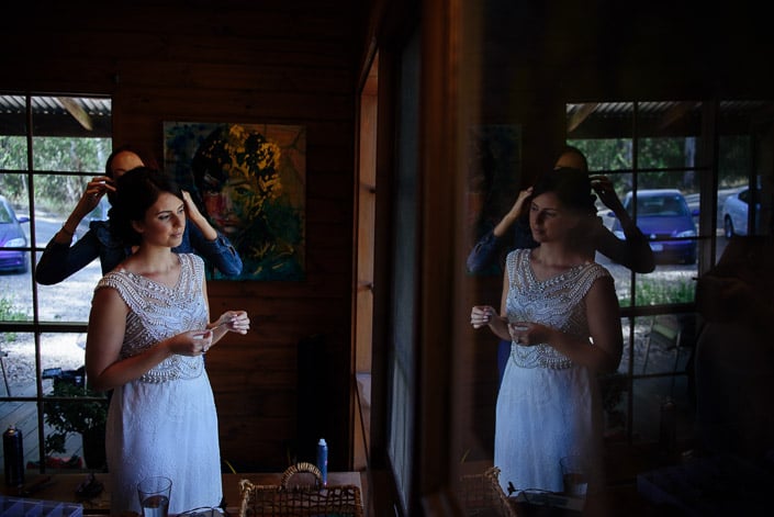 The bride and her reflection appear in a Pennyroyal Otways Retreat cottage window during hair styling