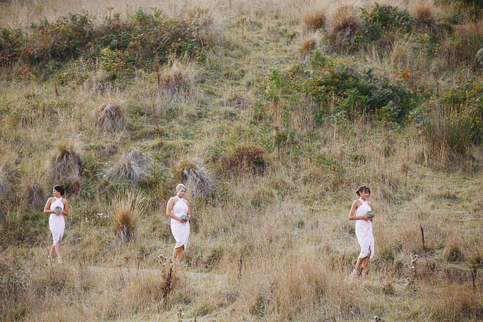 Three bridesmaids cross a tussock-covered slope at Pennyroyal Retreat with succulent posies