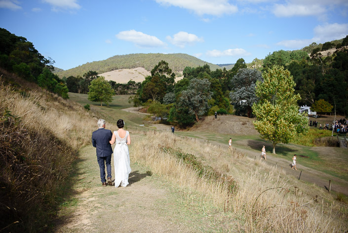 The bride and a silver-haired man follow the hillside path to the Pennyroyal Retreat ceremony