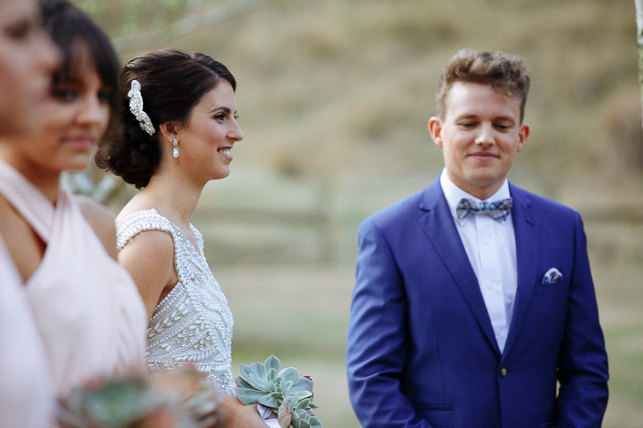 The bride's smile carries down the line as the groom blinks back a tear in his blue suit.