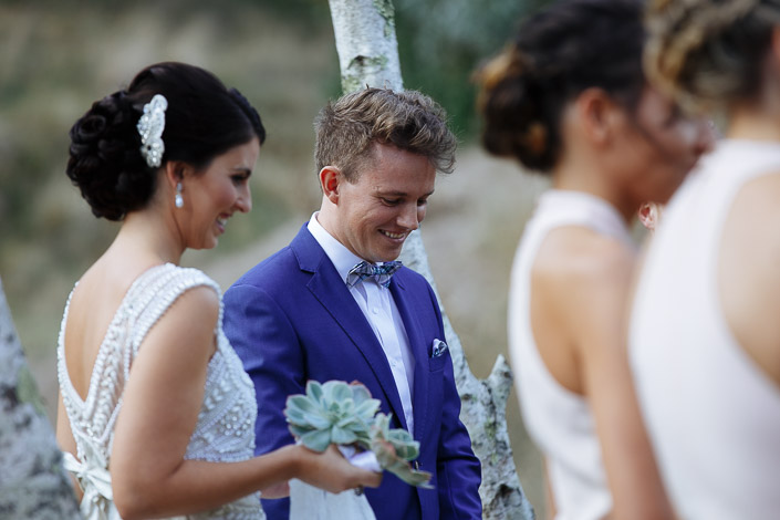 The groom grins at the succulent posy passed between him and the bride, bridesmaids in front.