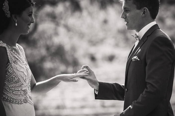 The bride's hand rests in the groom's for the ring, in black and white.