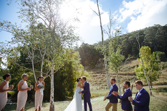 The couple share their first kiss as the wedding party applauds