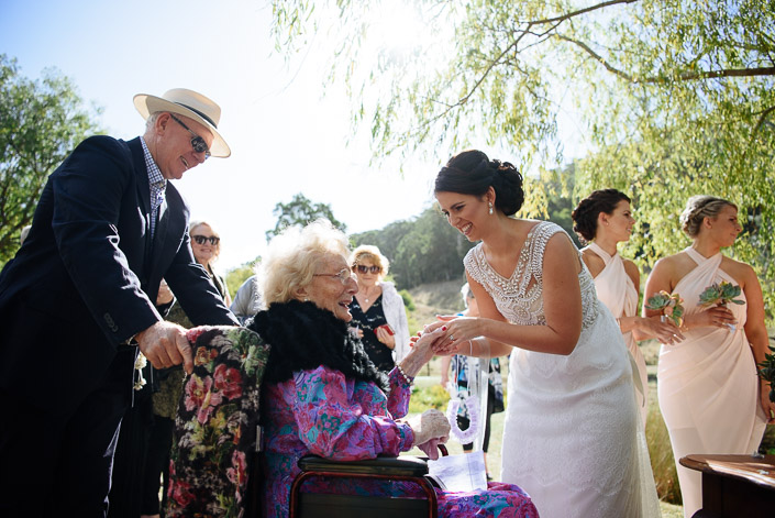 The bride shows her rings to a white-haired guest in a wheelchair
