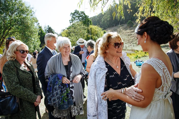 The bride laughs with a guest in a black sequinned dress and white coat