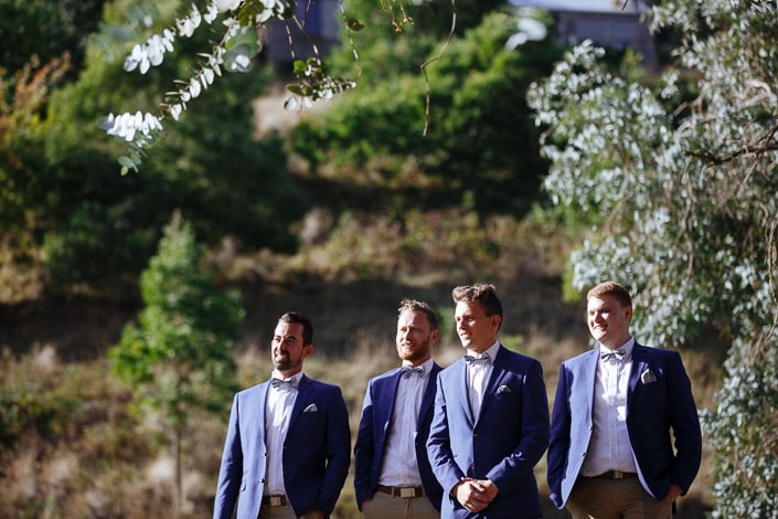 The groom stands with three groomsmen in blue wedding jackets