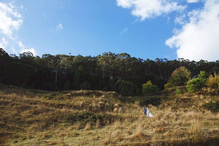 The couple appear small beneath a wide sky on the hillside at Pennyroyal Retreat