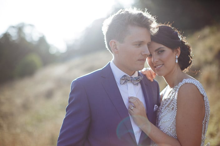 The bride's chin rests at the groom's shoulder, her ring bright against the navy lapel.