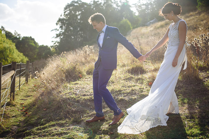 The groom leads the bride down a tussock-covered bank at Pennyroyal Retreat