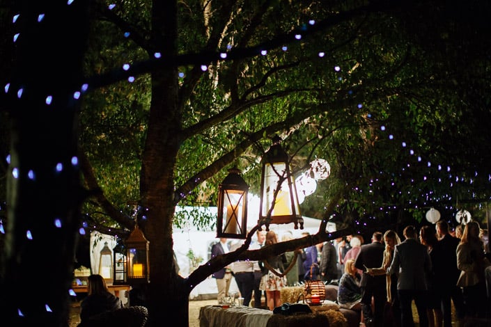 Lanterns hang from a fairy-lit tree above wedding guests at Pennyroyal Otways Retreat