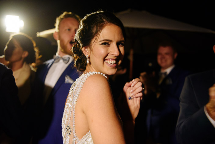An over-the-shoulder grin, hands clasped in the stage light