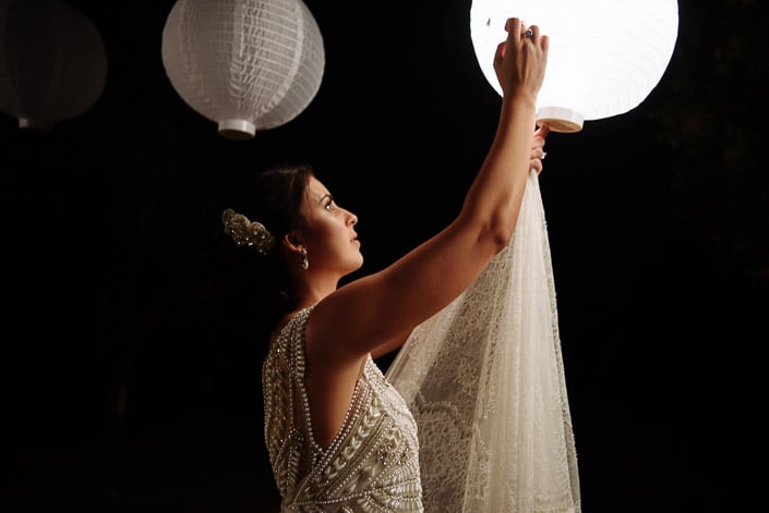 The bride reaches up to a glowing paper lantern at Pennyroyal Retreat