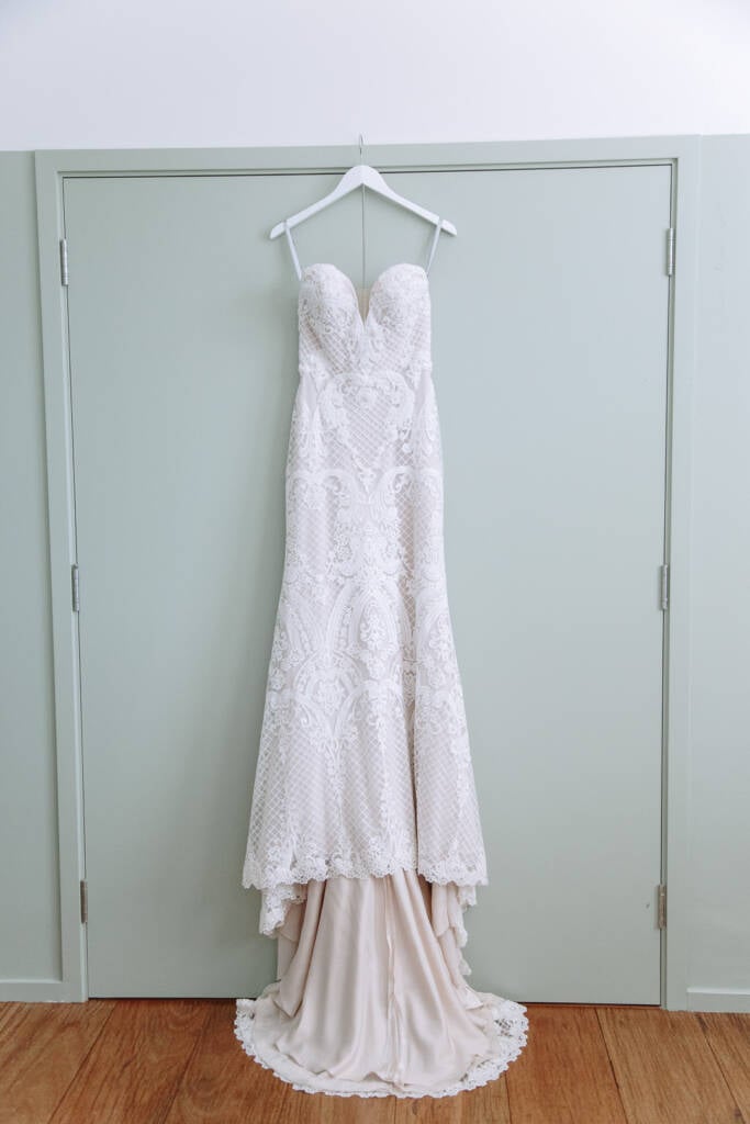 Georgia's lace wedding gown hangs against pale green doors at Prince Deck.
