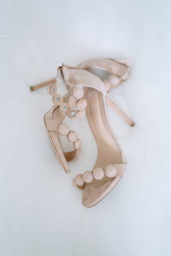 Pale open-toe bridal heels with circular strap details rest on white fabric.