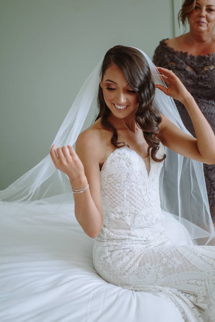 Georgia holds her veil while seated on a white bed at The Prince Deck.