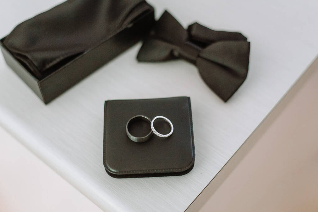 Two rings rest beside a black bow tie and an open ring box.