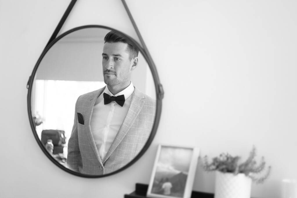 Black-and-white reflection of Michael in a round mirror at home, wearing his grey jacket and bow tie.