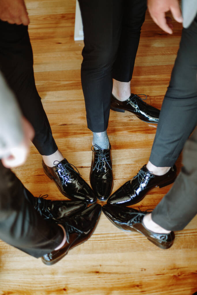 Polished black lace-up wedding shoes rest on a timber floor.