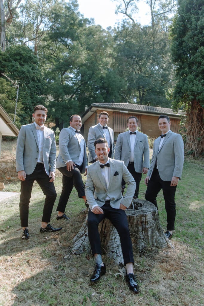 Michael sits on a tree stump at home with five attendants standing behind him.