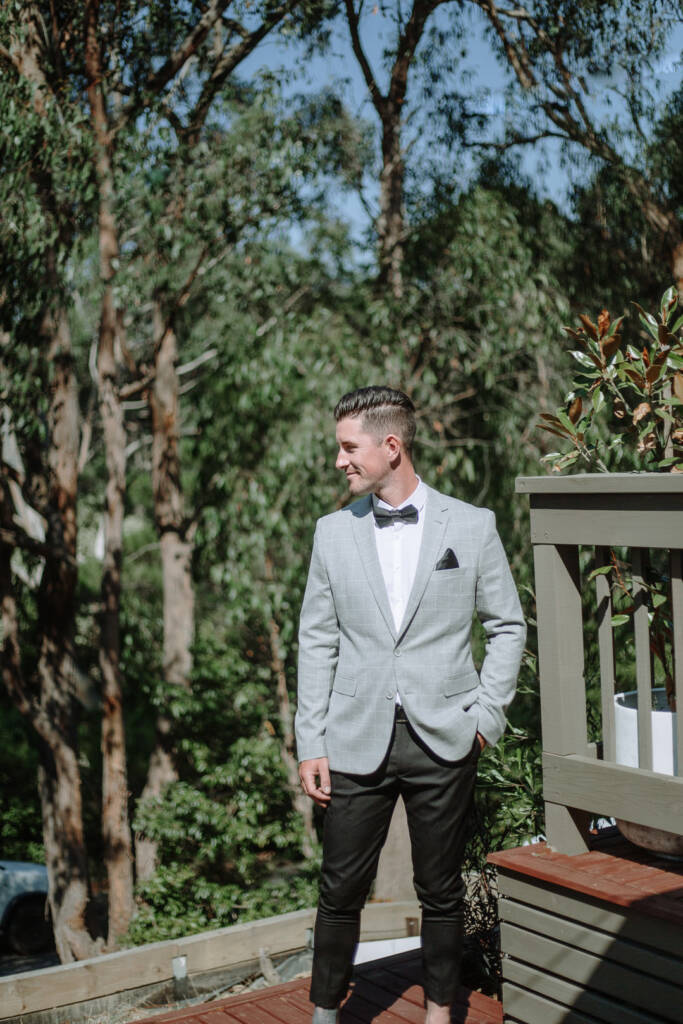 Michael stands beside a timber railing at home, with leafy trees behind him.