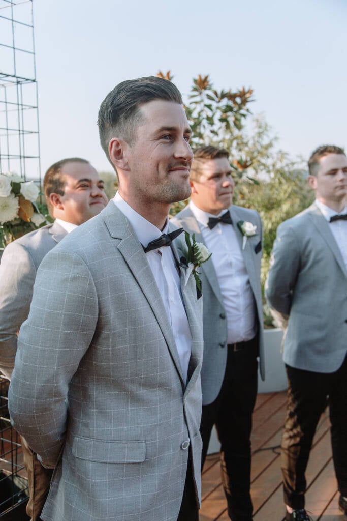 Michael smiles towards the aisle beside the white-flowered arbour at The Prince Deck.