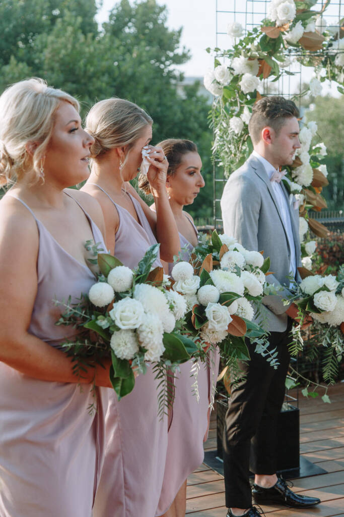 A bridesmaid dabs her eye beside the white-flowered arbour at Prince Deck.