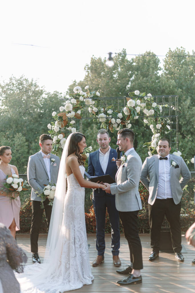 Georgia and Michael hold hands while their celebrant addresses the ceremony at Prince Deck.