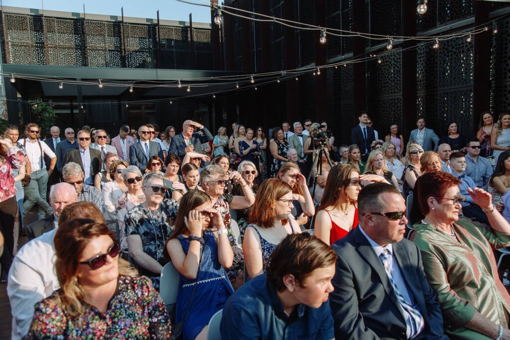 Guests watch the rooftop wedding ceremony beneath festoon lights and geometric screens at The Prince Deck.
