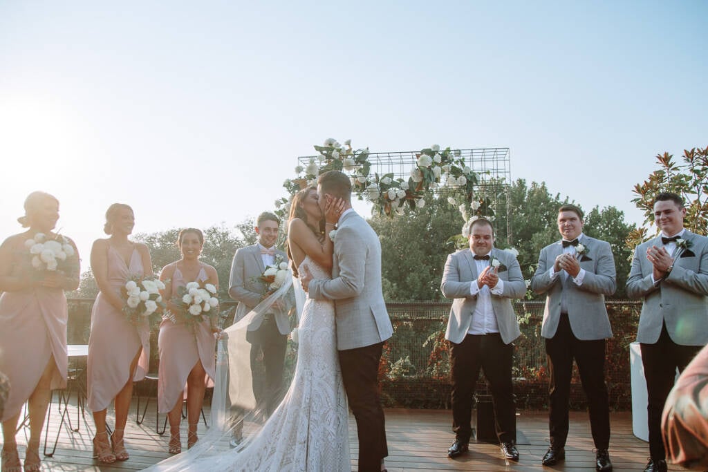Georgia and Michael kiss beneath the white-flowered arbour at Prince Deck.