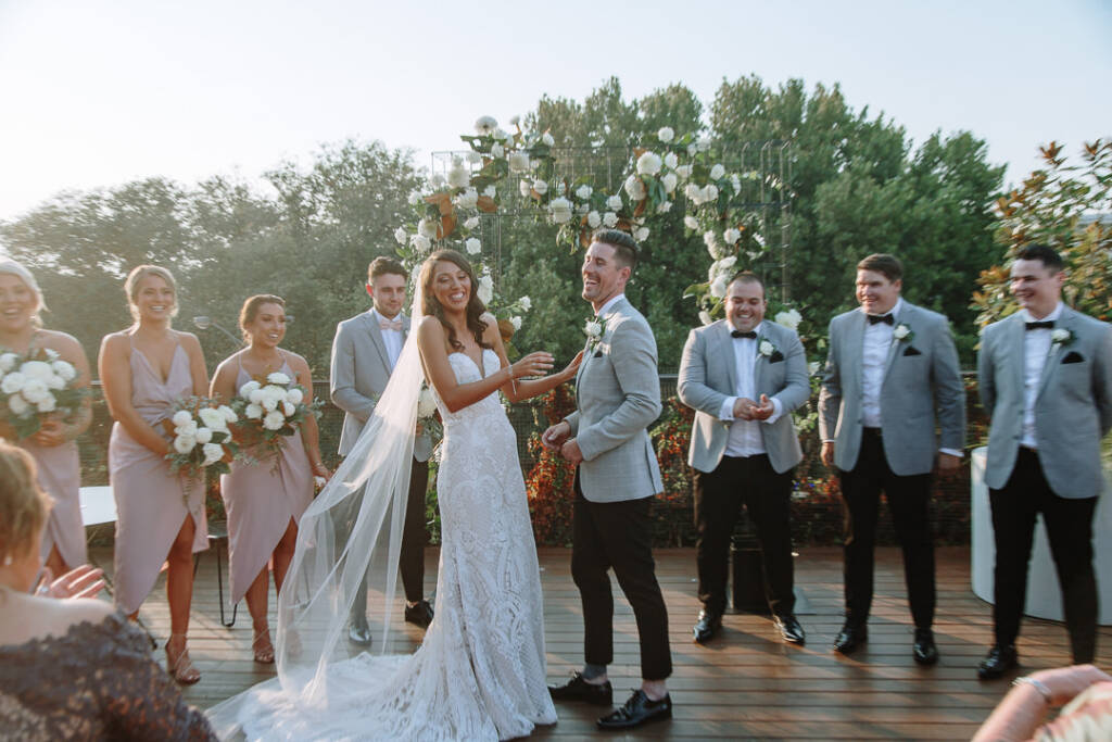 Georgia and Michael laugh with their wedding party beside the arbour at The Prince Deck.