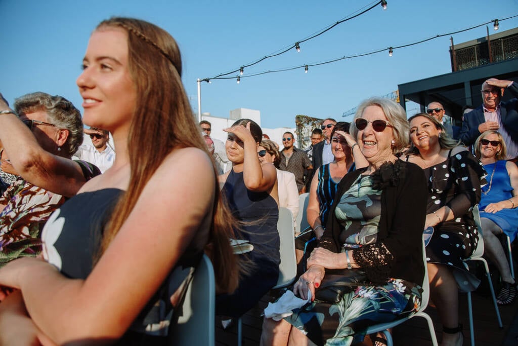 Seated guests smile and shade their eyes during the ceremony at Prince Deck.