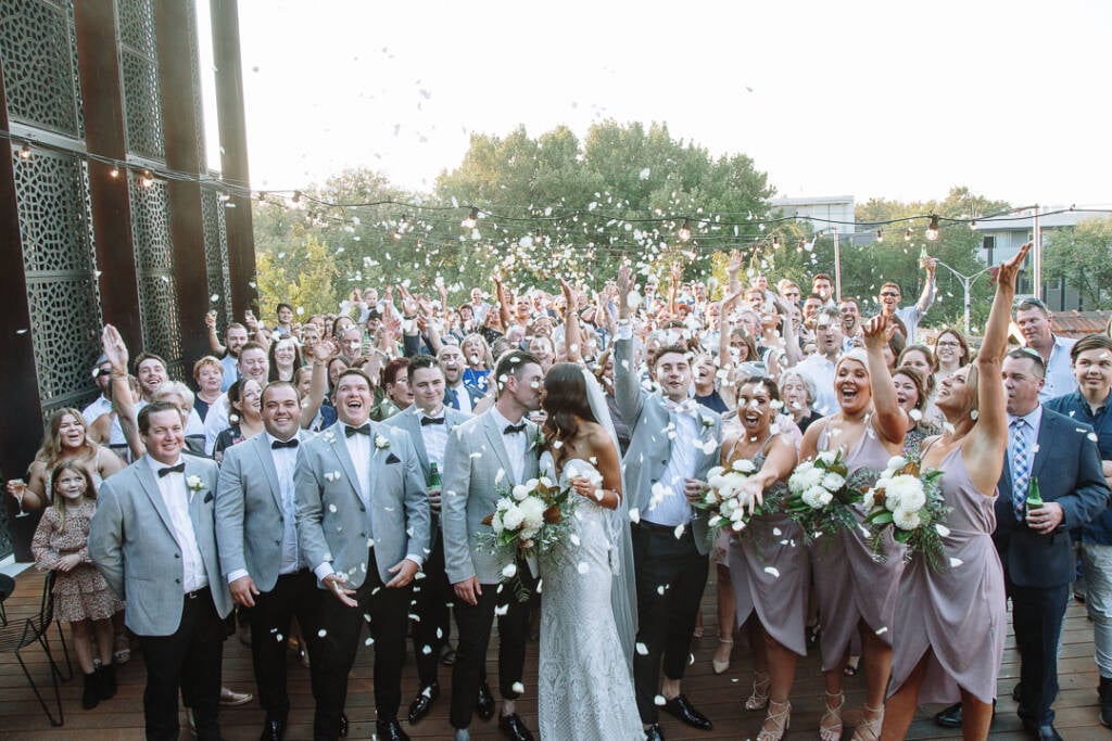 Georgia and Michael kiss as guests throw petals during a group photo at The Prince Deck.