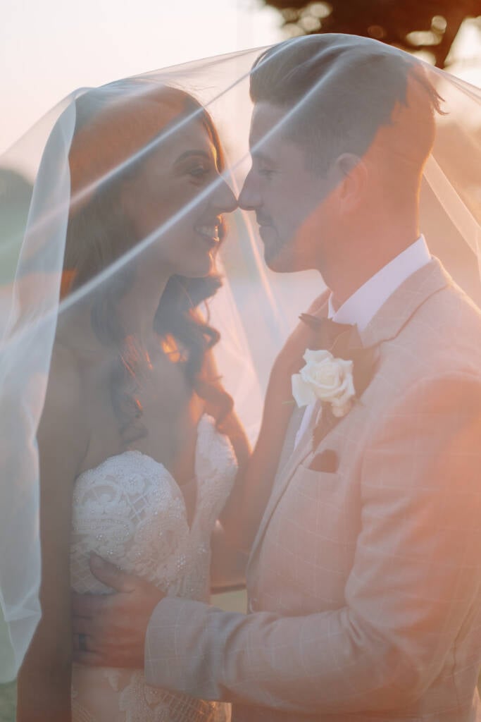 Georgia and Michael smile with their noses touching beneath her veil.