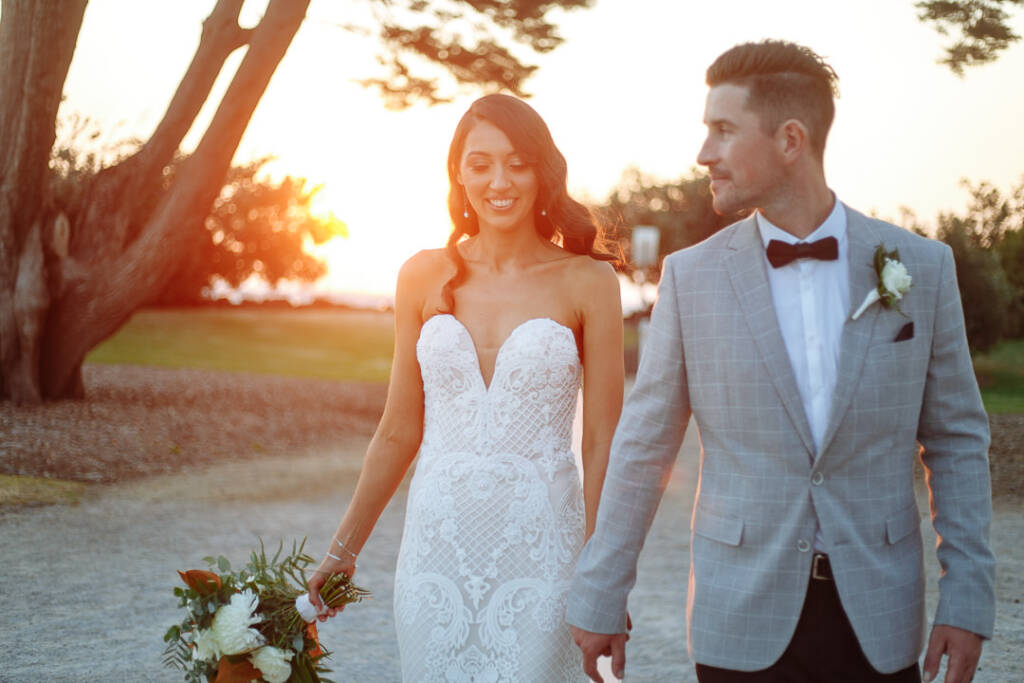 Georgia and Michael walk along a tree-lined path at Catani Gardens in the evening light.