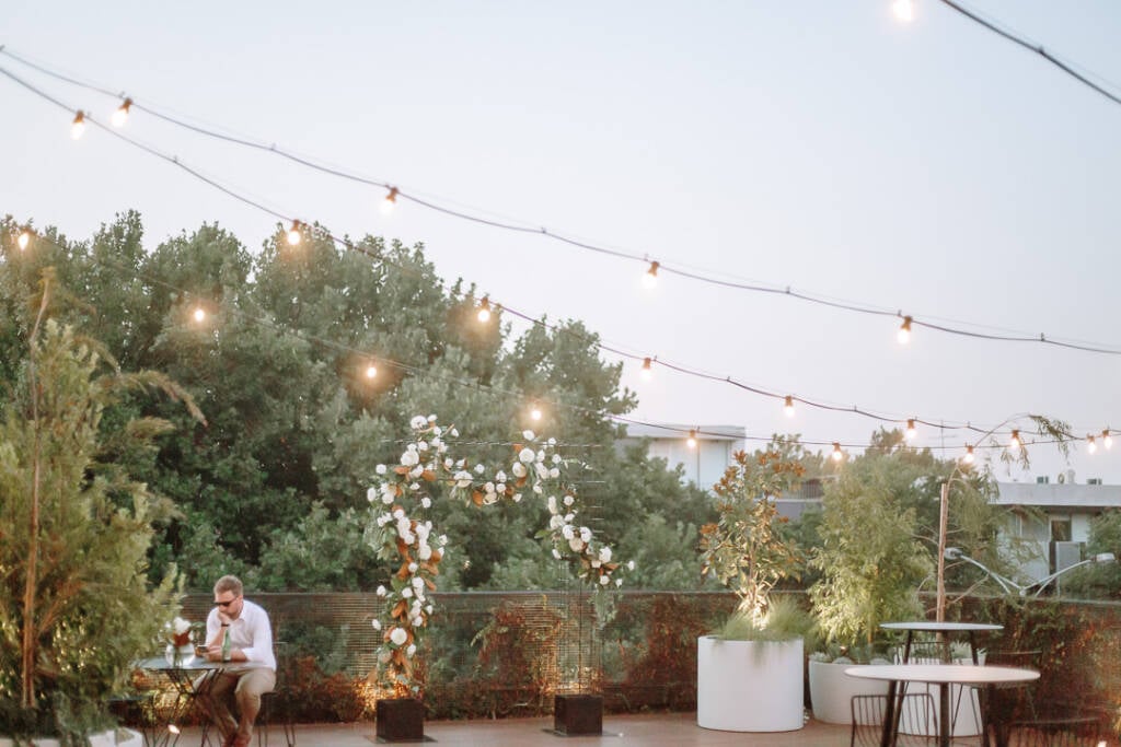 The floral arbour and cocktail tables sit beneath glowing festoon lights at Prince Deck at dusk.