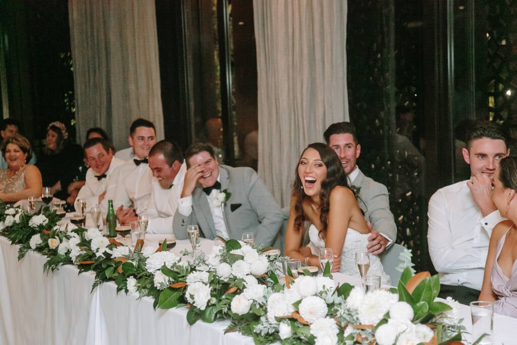 Georgia laughs with Michael and their wedding party at the flower-lined table at The Prince Deck.