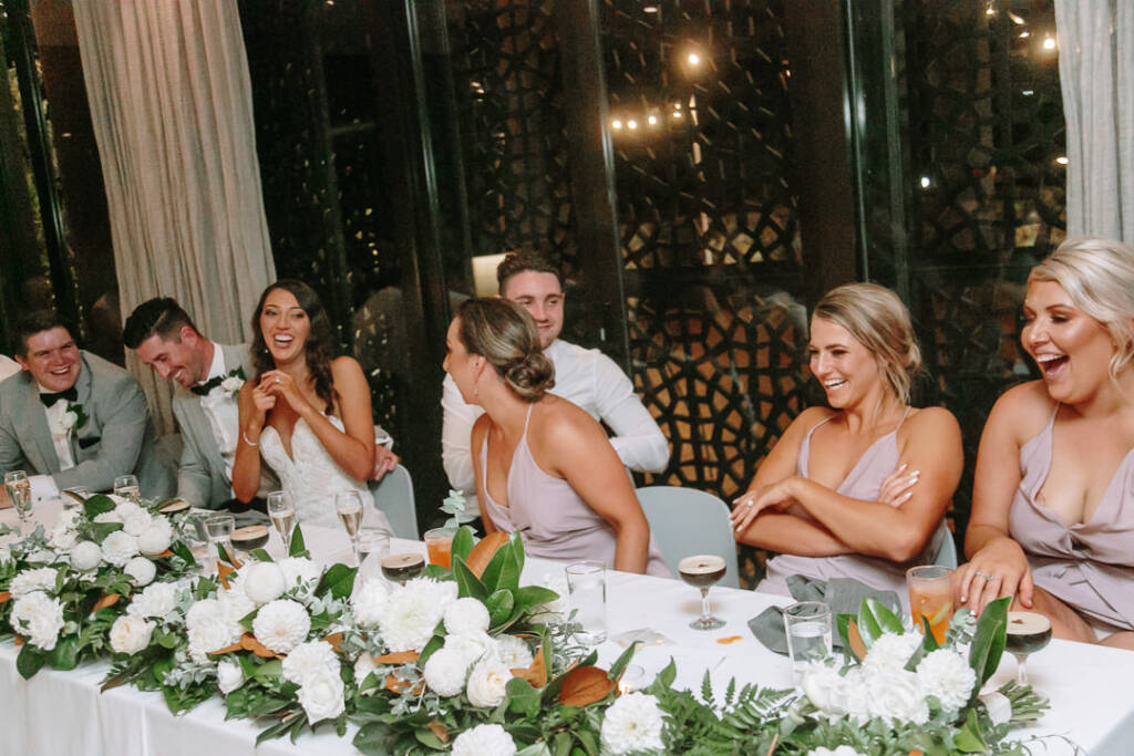 The wedding party laughs behind white flowers and foliage at Prince Deck.