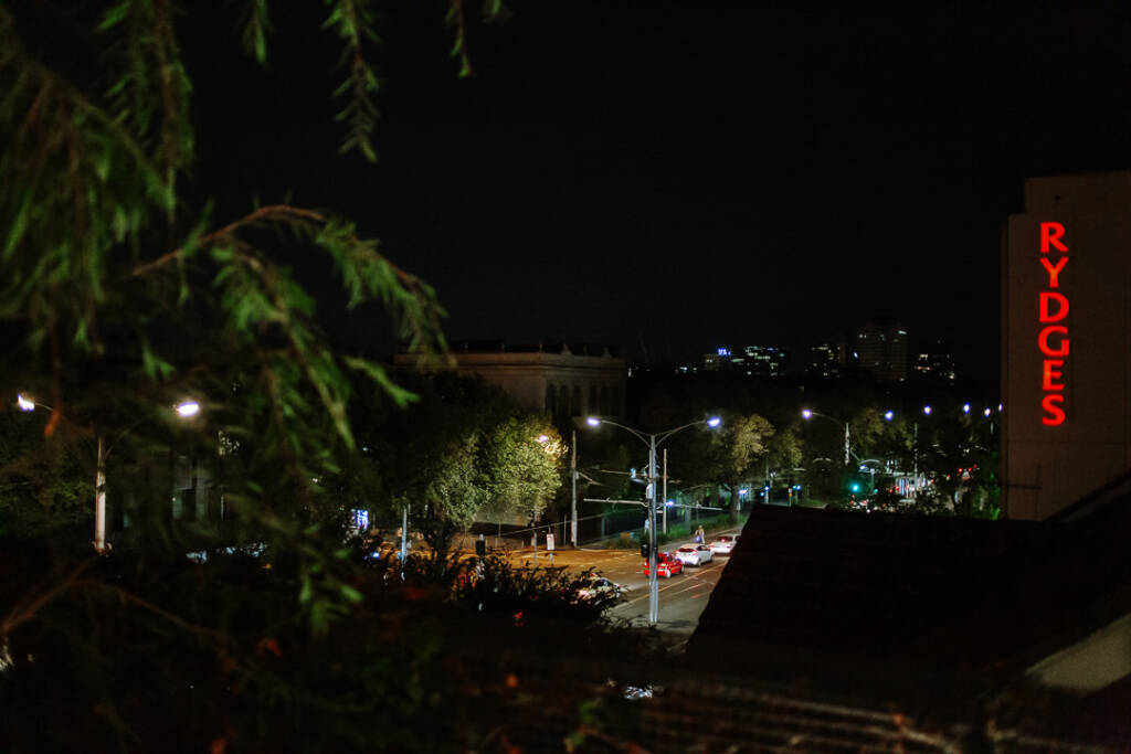 Night view from Prince Deck's open rooftop balcony across nearby rooftops and a lit street.