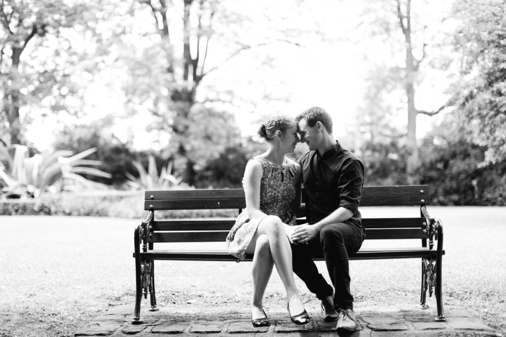 A casually dressed couple touch foreheads on a timber bench at Canterbury Gardens.