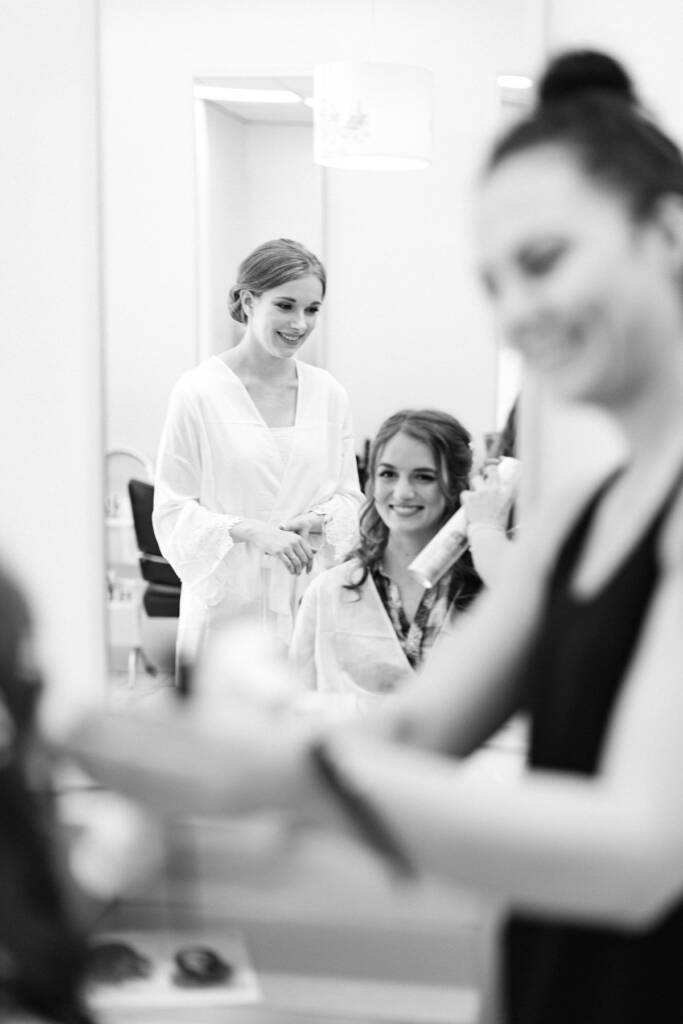 Sue smiles in her robe as a stylist sprays another person's hair at her parents' home.