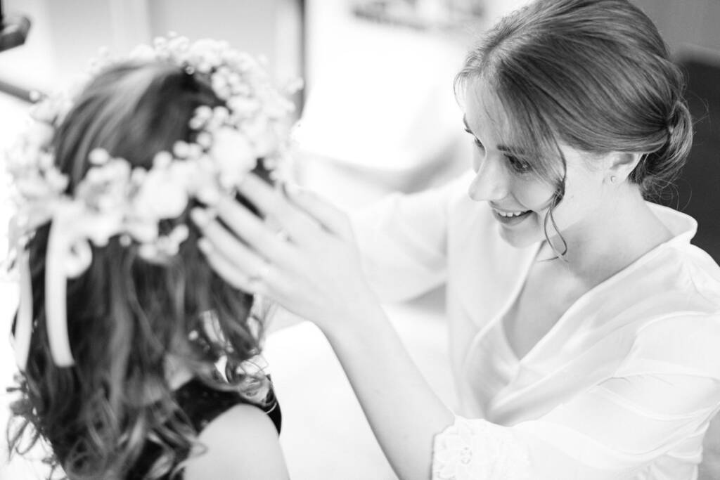 Sue in her robe settles a baby's breath flower crown on the flower girl's curls.