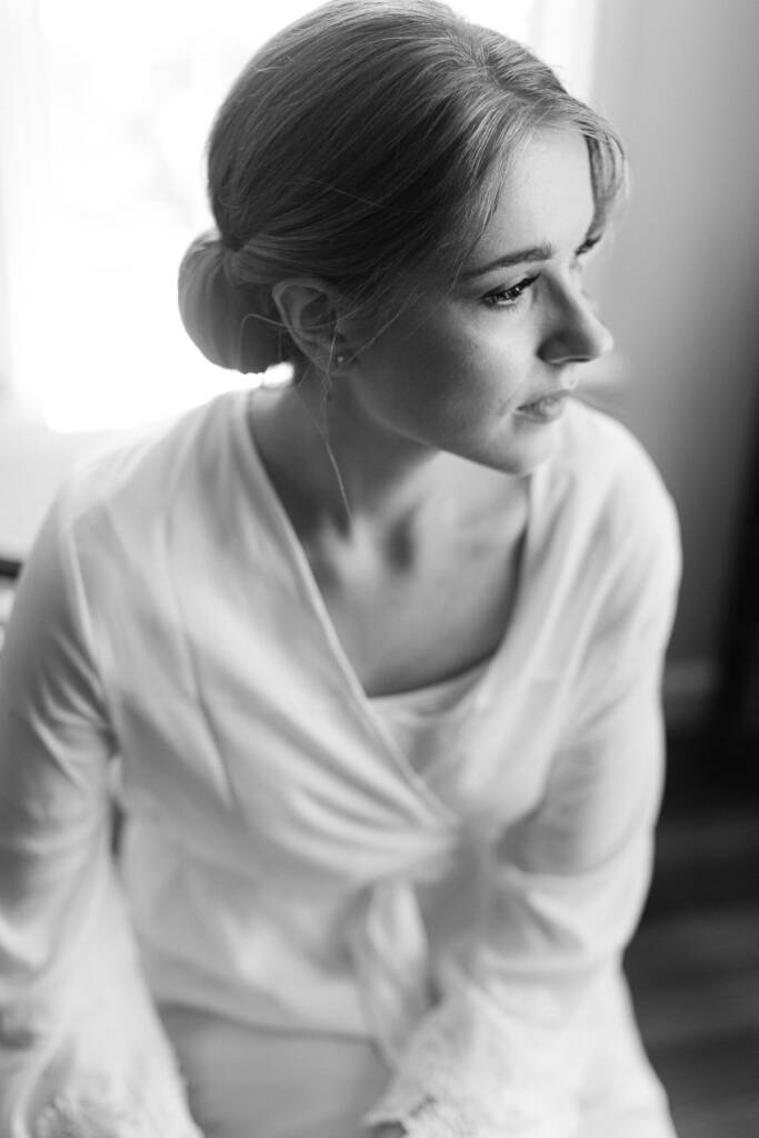 From above, Sue in a satin robe looks to the right, chignon lit by the window.