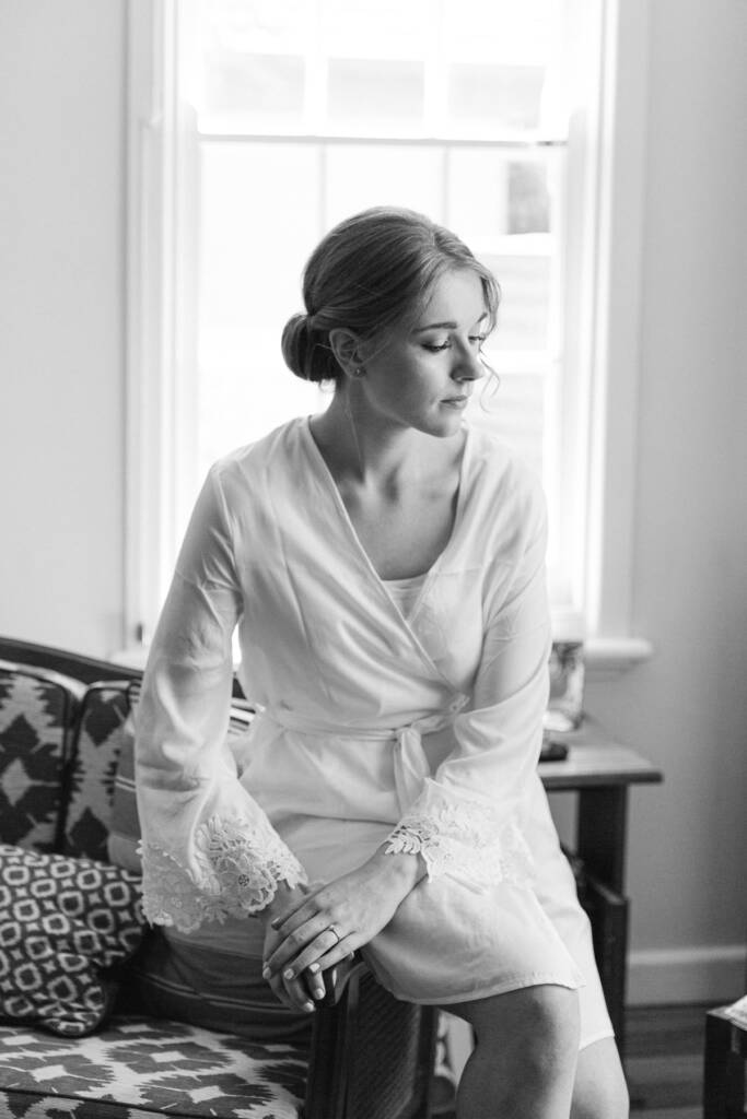 Perched on the arm of a patterned sofa, Sue in her lace cuffed robe looks down.