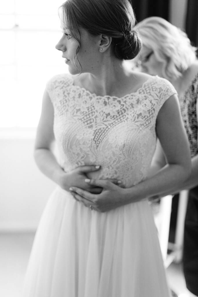 Sue stands in her lace gown while an attendant adjusts the dress behind her.