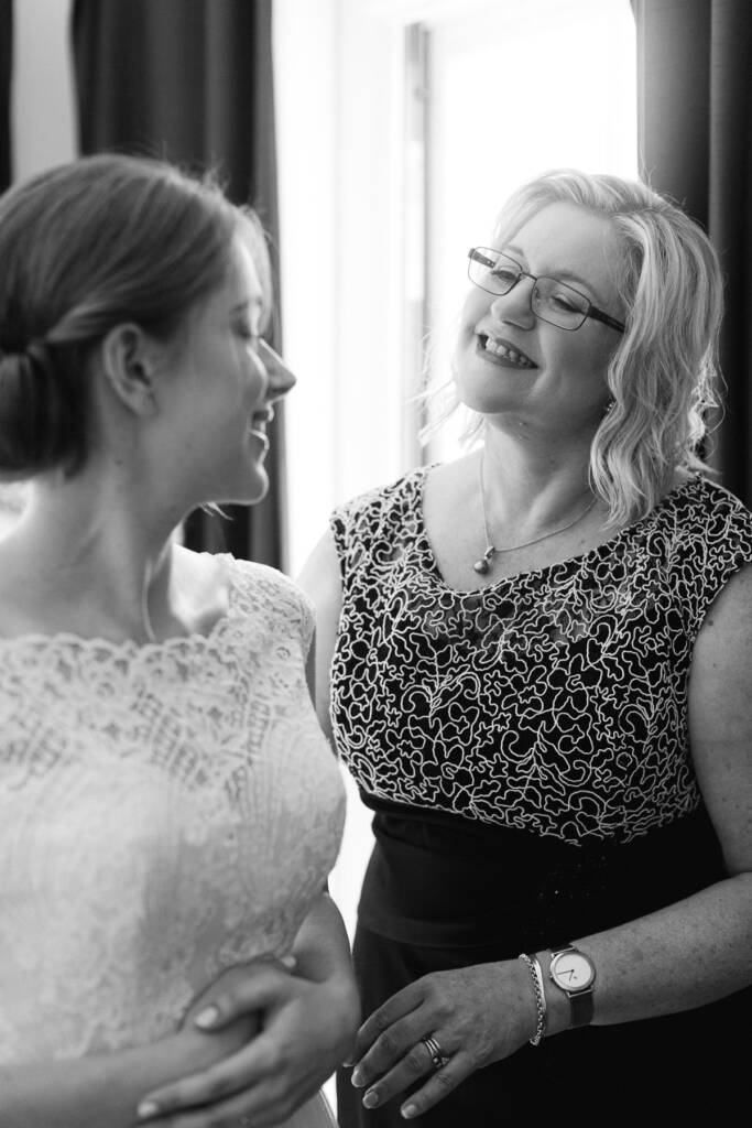 Sue laughs down at a laughing woman in glasses whose hands rest on her waist.